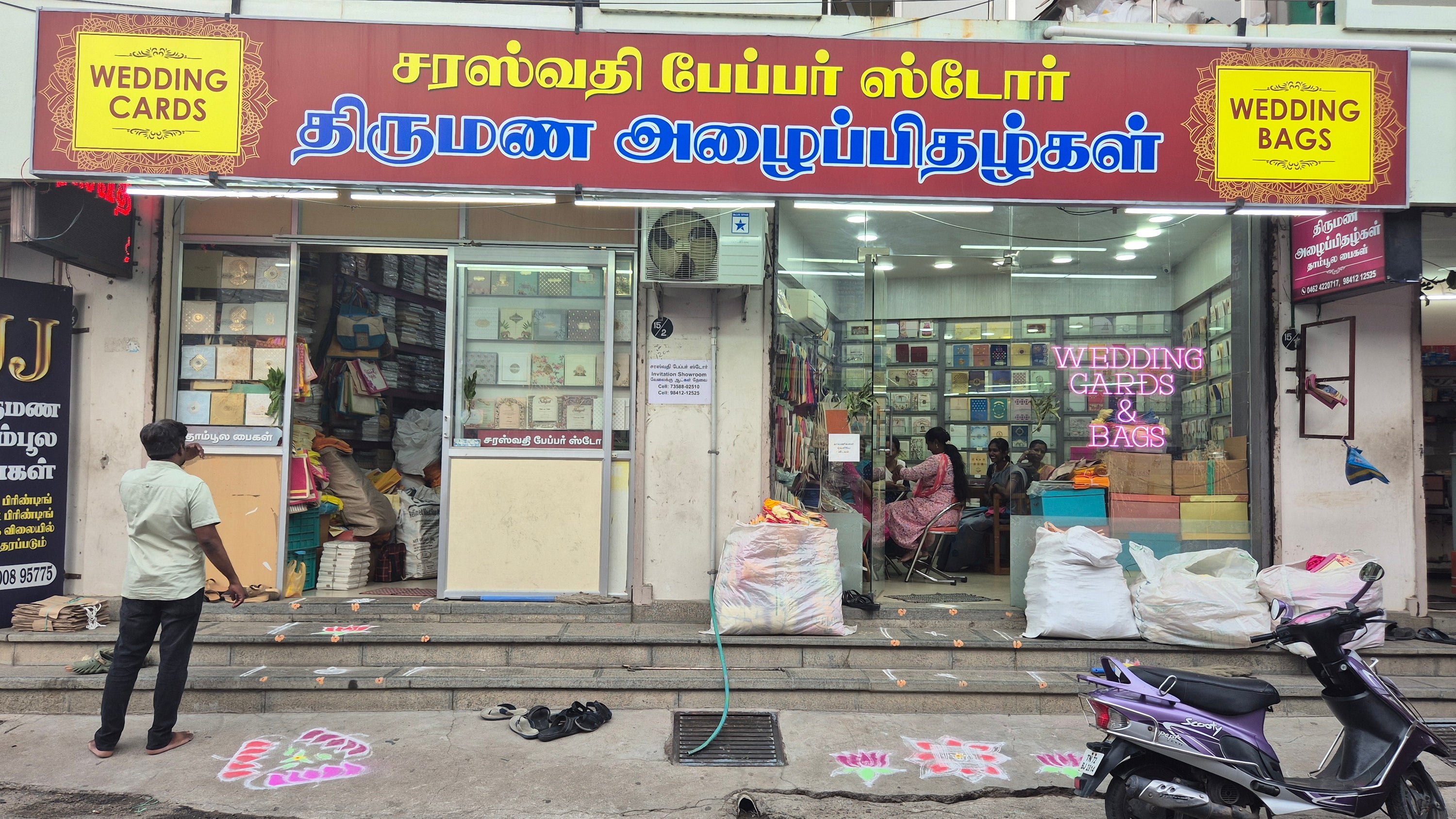Shopfront with 'Wedding Cards' and 'Wedding Bags' signs, people inside, and a parked scooter outside.